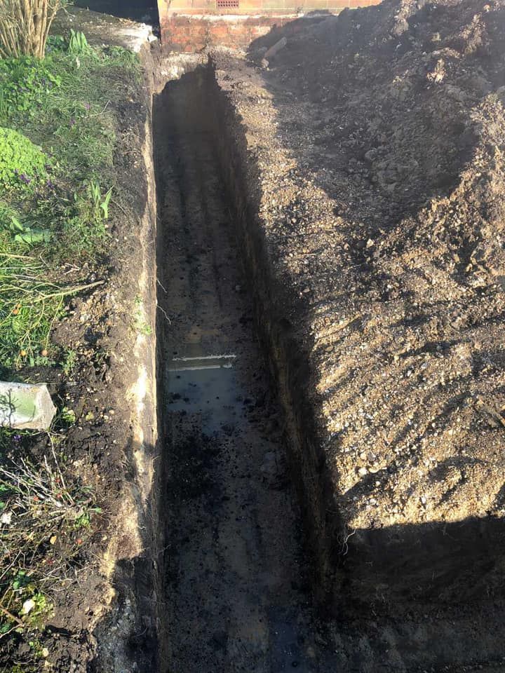 A trench is being dug in the dirt next to a brick wall.