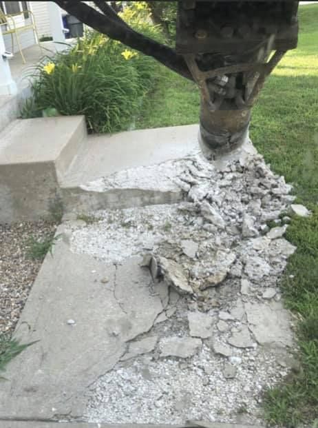A concrete sidewalk is being demolished by a machine.