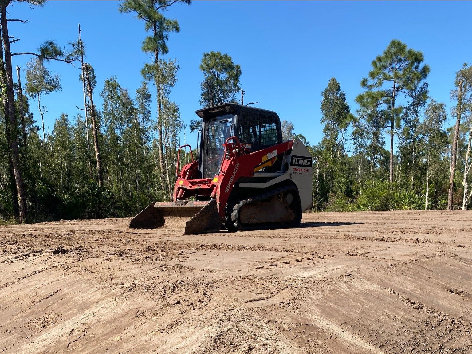 A bulldozer is driving through a dirt field with trees in the background.