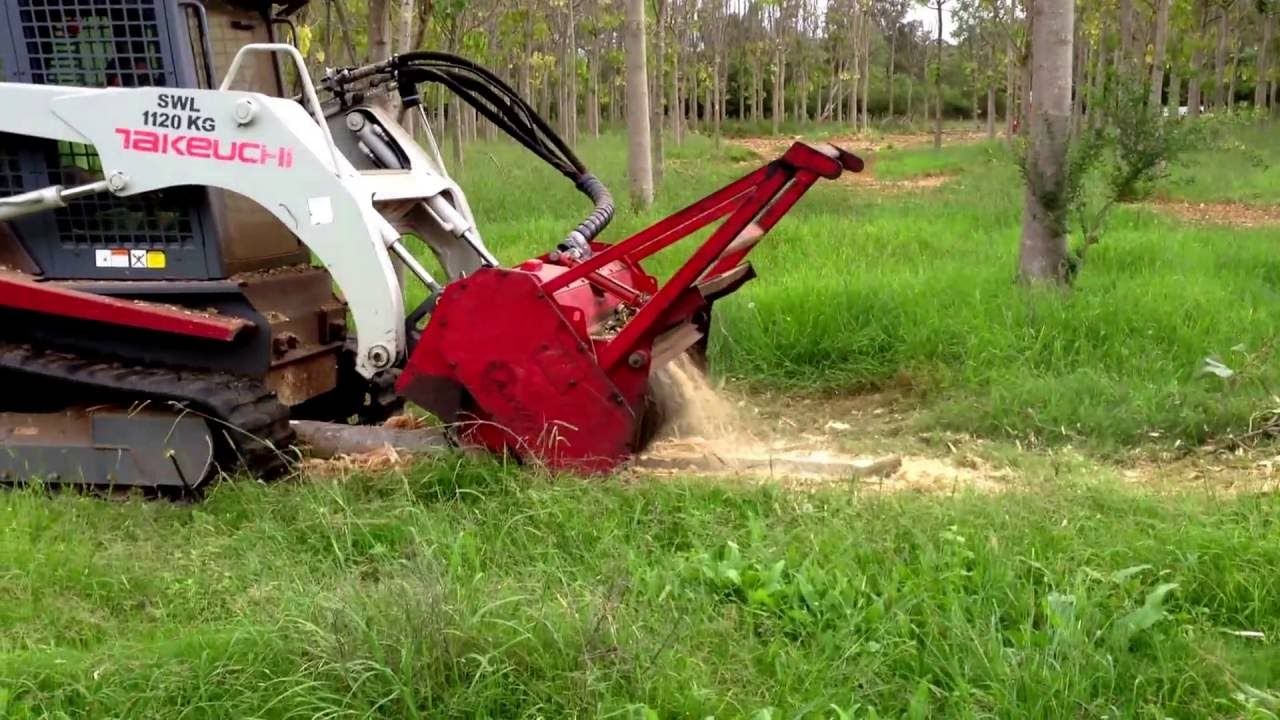 A bulldozer is cutting a tree stump in the grass.