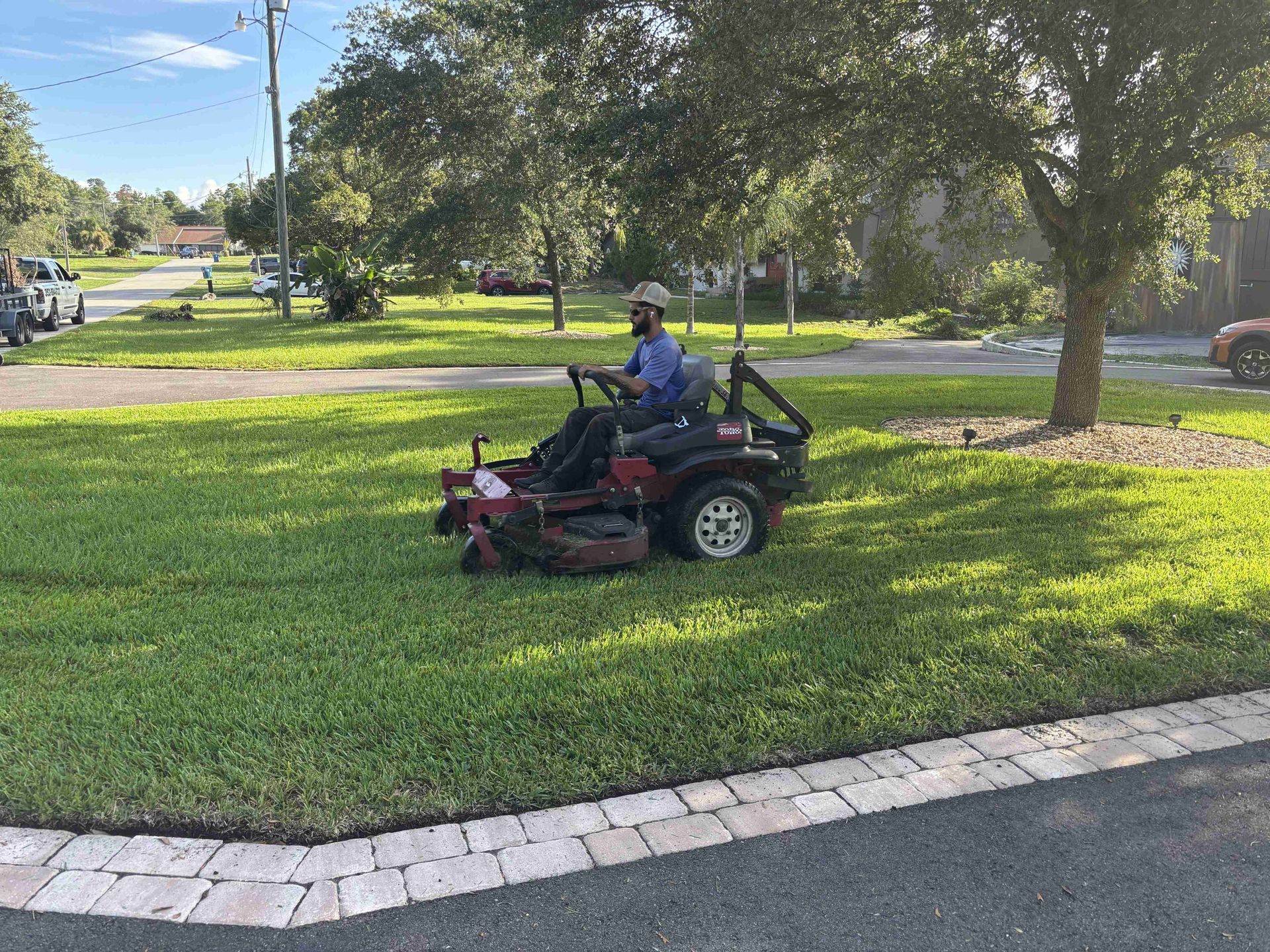 Person mowing a lawn with a red zero-turn mower on a sunny day.