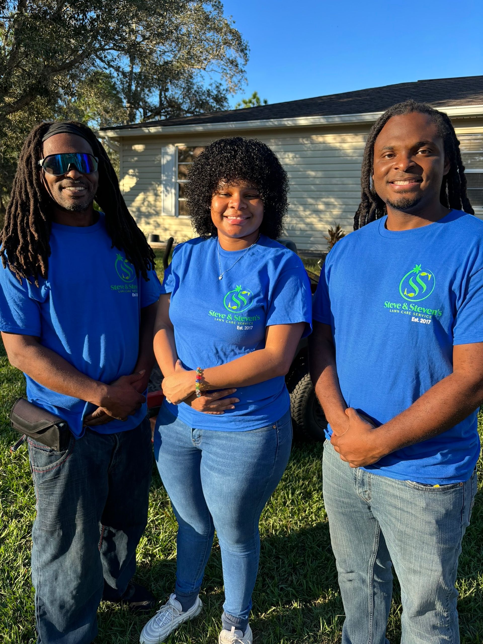 Three people wearing blue shirts are standing next to each other in front of a house.
