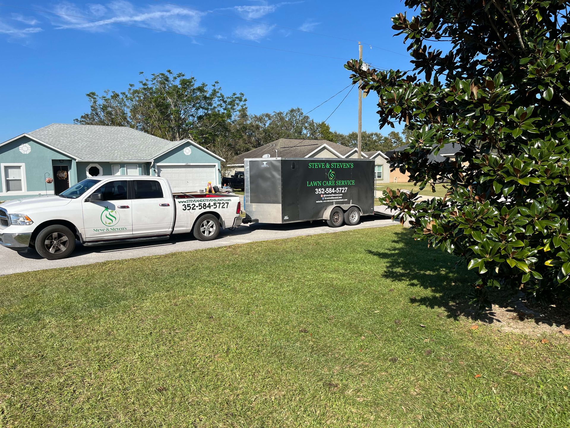 A white truck with a trailer attached to it is parked in front of a house.
