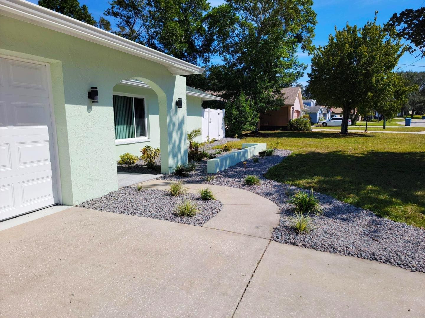 A green house with a white garage door and a walkway