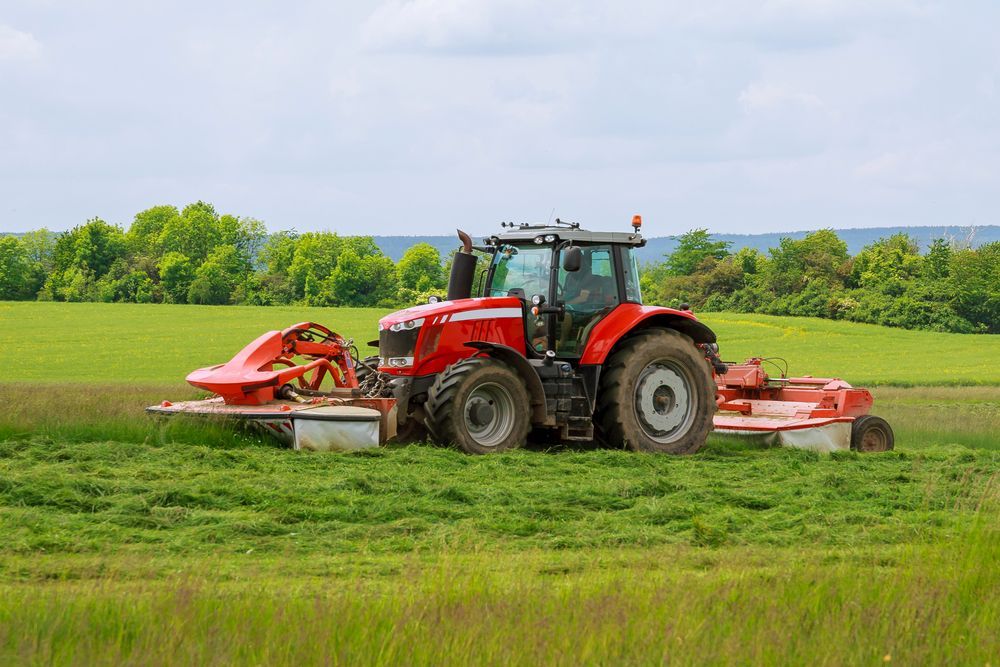 Red Tractor Mowing Grass in a Field; Trees in Background — Ace Clearing & Mulching In Forster, NSW