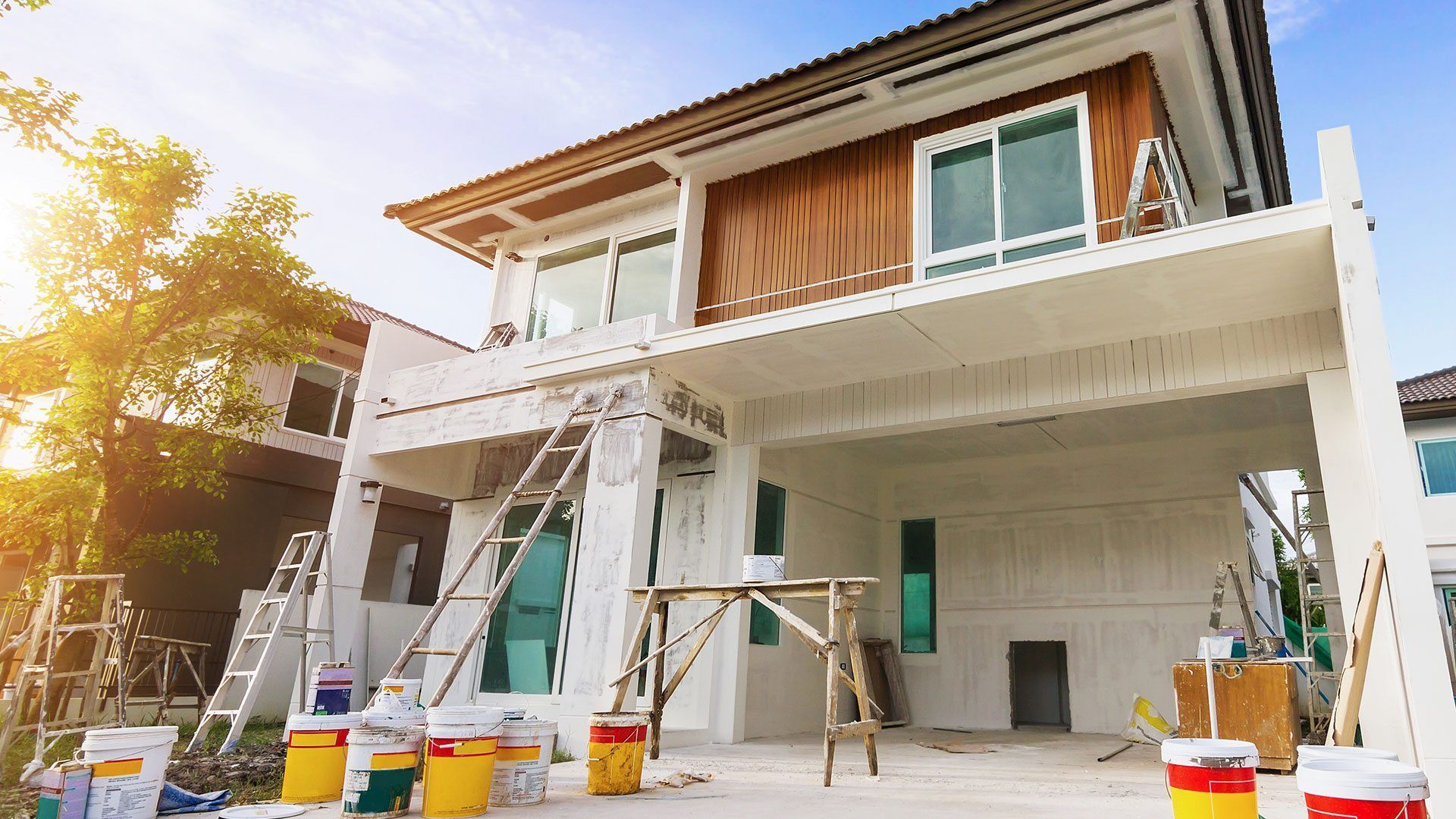 House exterior under construction, with ladders, paint buckets, and scaffolding.