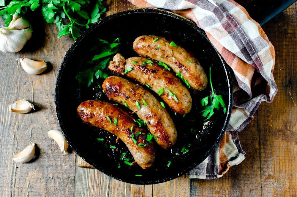 Four Sausages Are Cooking In A Skillet On A Wooden Table — McGrath Meats In Taree, NSW