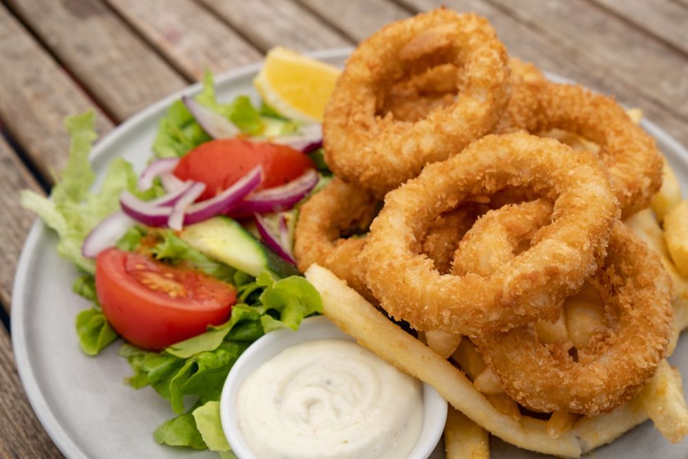 A Plate Of Fried Onion Rings With French Fries And A Salad On A Wooden Table — McGrath Meats In Taree, NSW