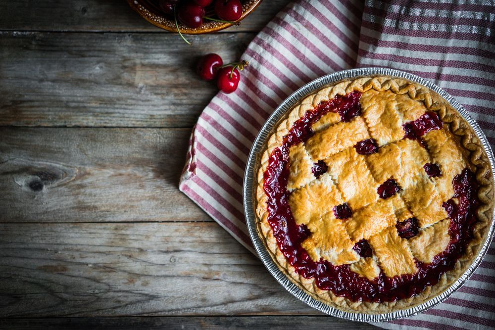 A Cherry Pie Is Sitting On A Wooden Table Next To A Basket Of Cherries — McGrath Meats In Taree, NSW