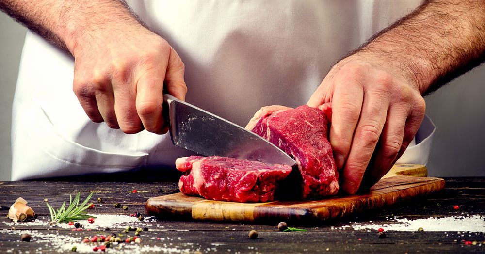 A Man Is Cutting A Piece Of Meat On A Cutting Board — McGrath Meats In Taree, NSW