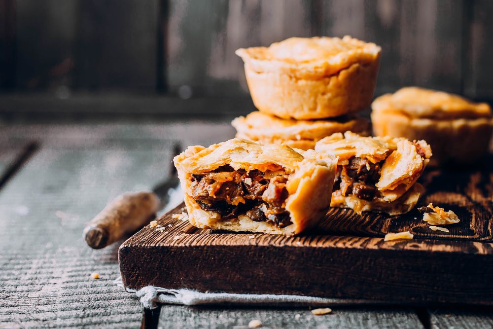 Three Pies Are Stacked On Top Of Each Other On A Wooden Cutting Board — McGrath Meats In Taree, NSW