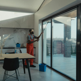 Modern kitchen with island seating and large glass doors opening to a balcony, cleaner at work