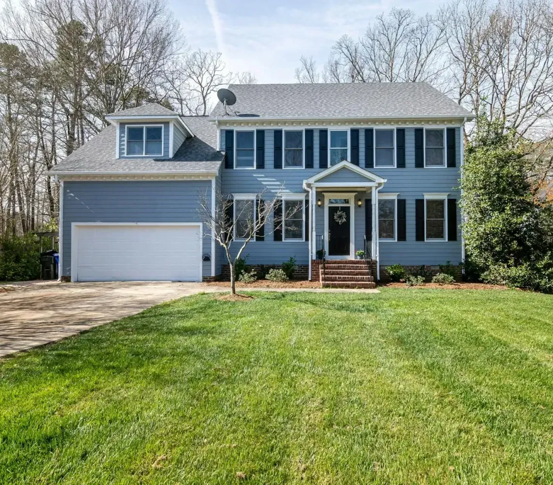 Blue two-story suburban house with white trim, front porch, attached garage, and a large green lawn