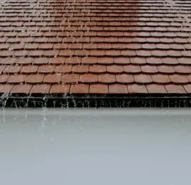 Snow sliding off a red-tiled roof above a white wall