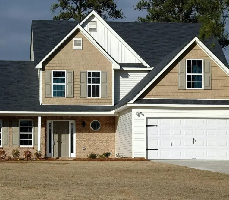 Suburban two-story beige house with a white garage and dark roof on a bare lot
