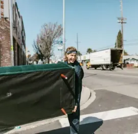 Person holding a large green tarp at a street corner on a sunny day