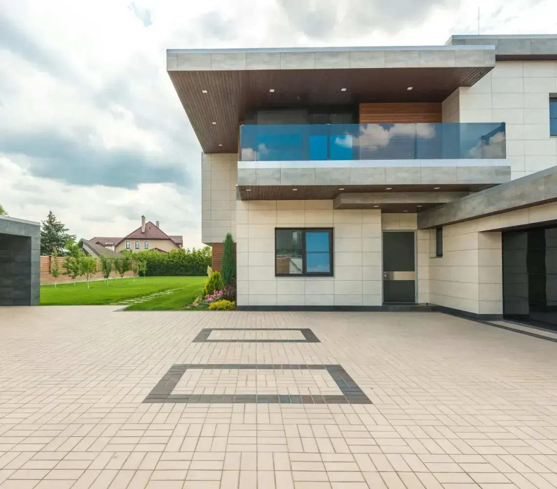 Modern two-story house with a large paved driveway and a garage under a cloudy sky