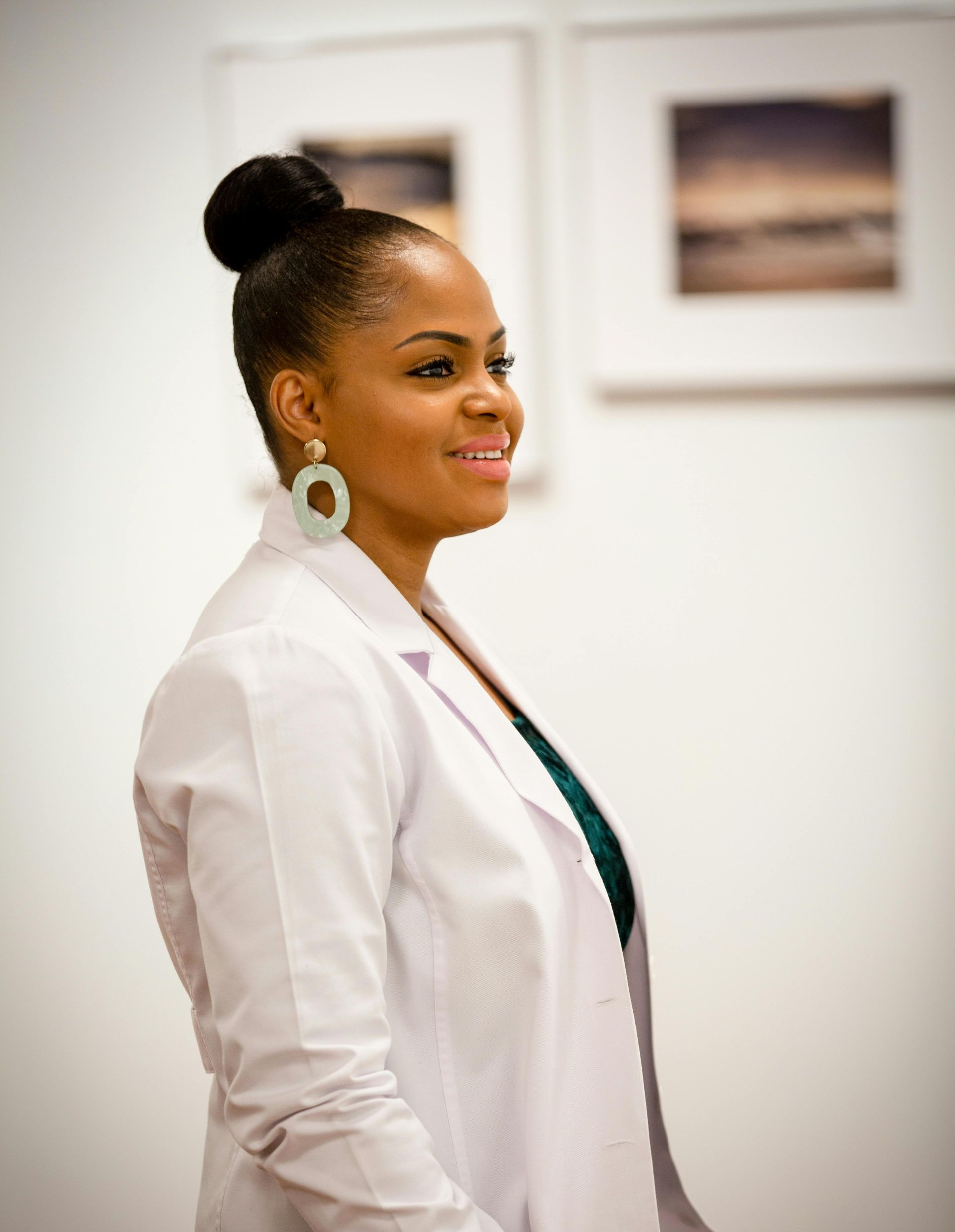 Woman in a white blazer smiling in a bright indoor setting with framed wall art.