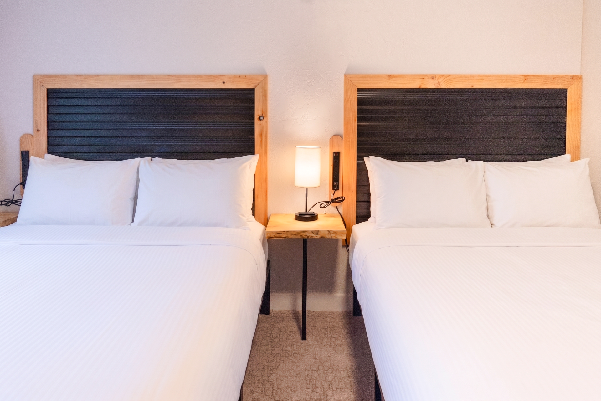 Two neatly made twin beds with dark headboards and a bedside lamp in a hotel-style room
