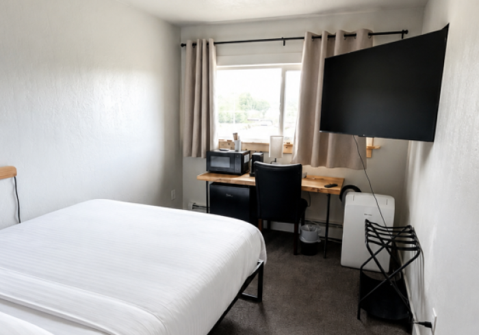 Small bedroom with twin bed, desk by window, and wall-mounted TV on the right.