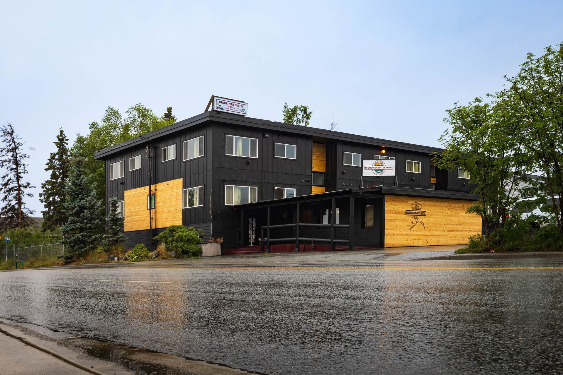 Modern black-and-wood building on a rainy street under a cloudy sky