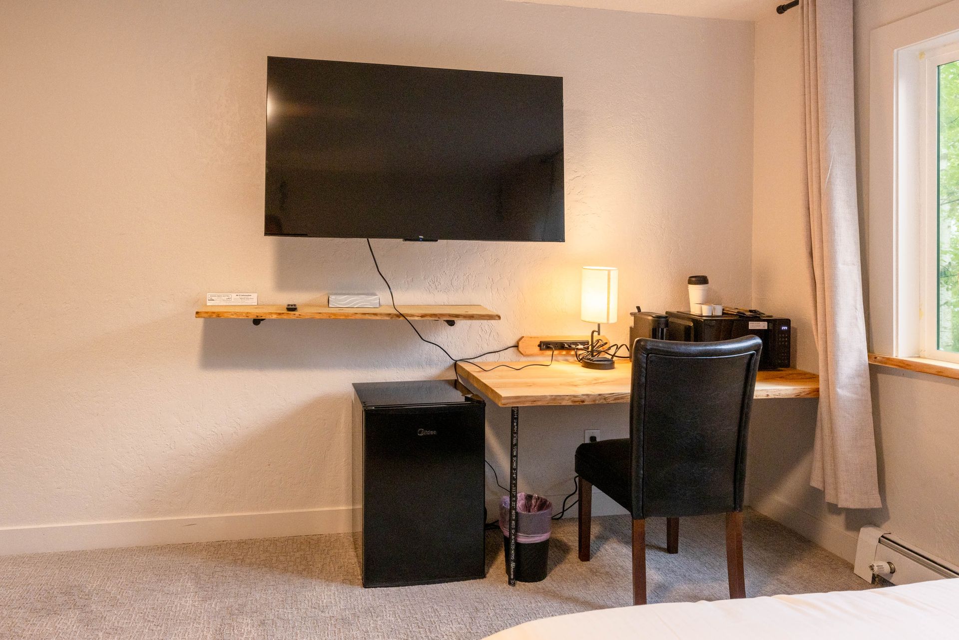 Desk setup with wall-mounted TV, lamp, chair, and computer in a small room