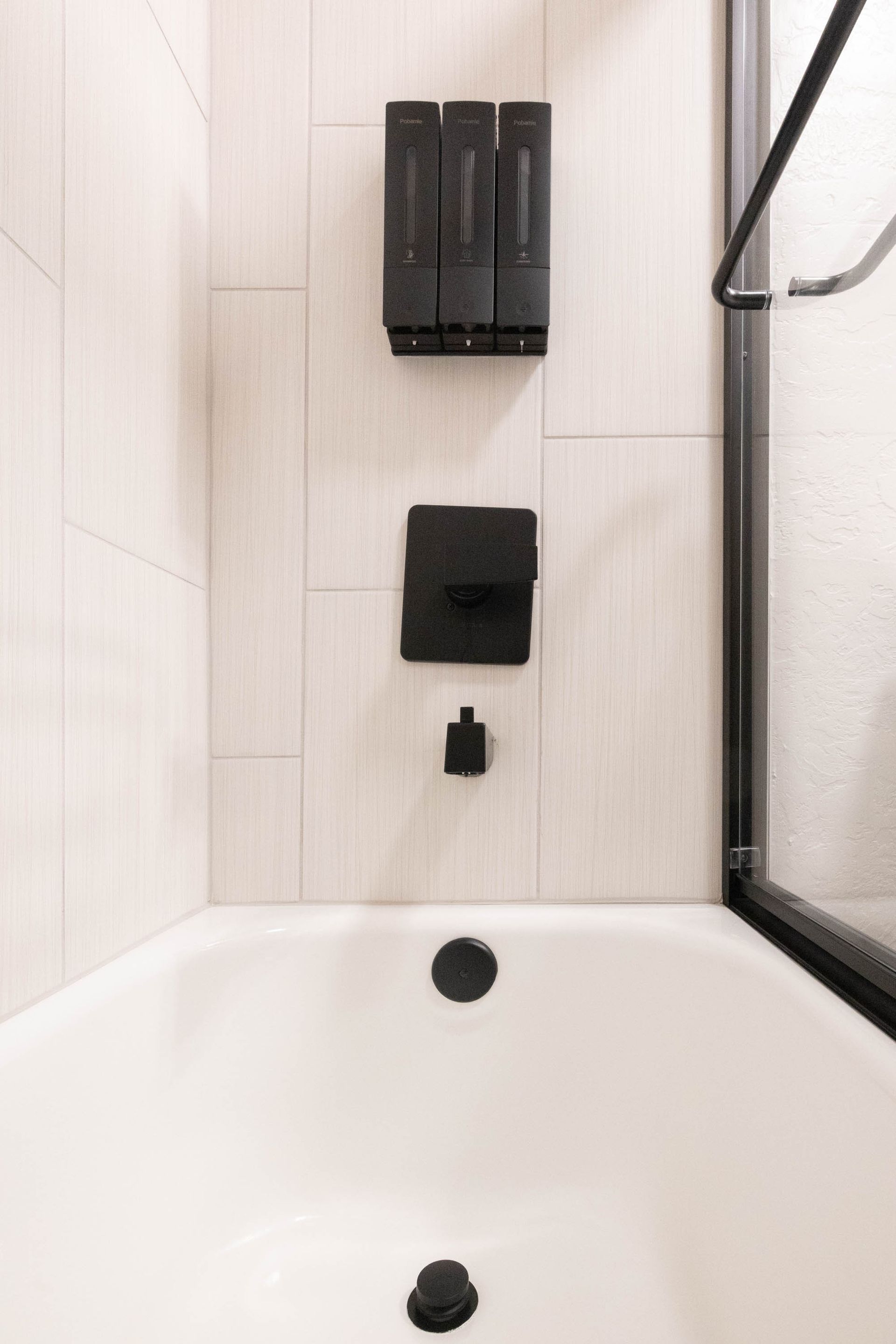 Modern white bathtub with black fixtures and shower controls in a tiled bathroom