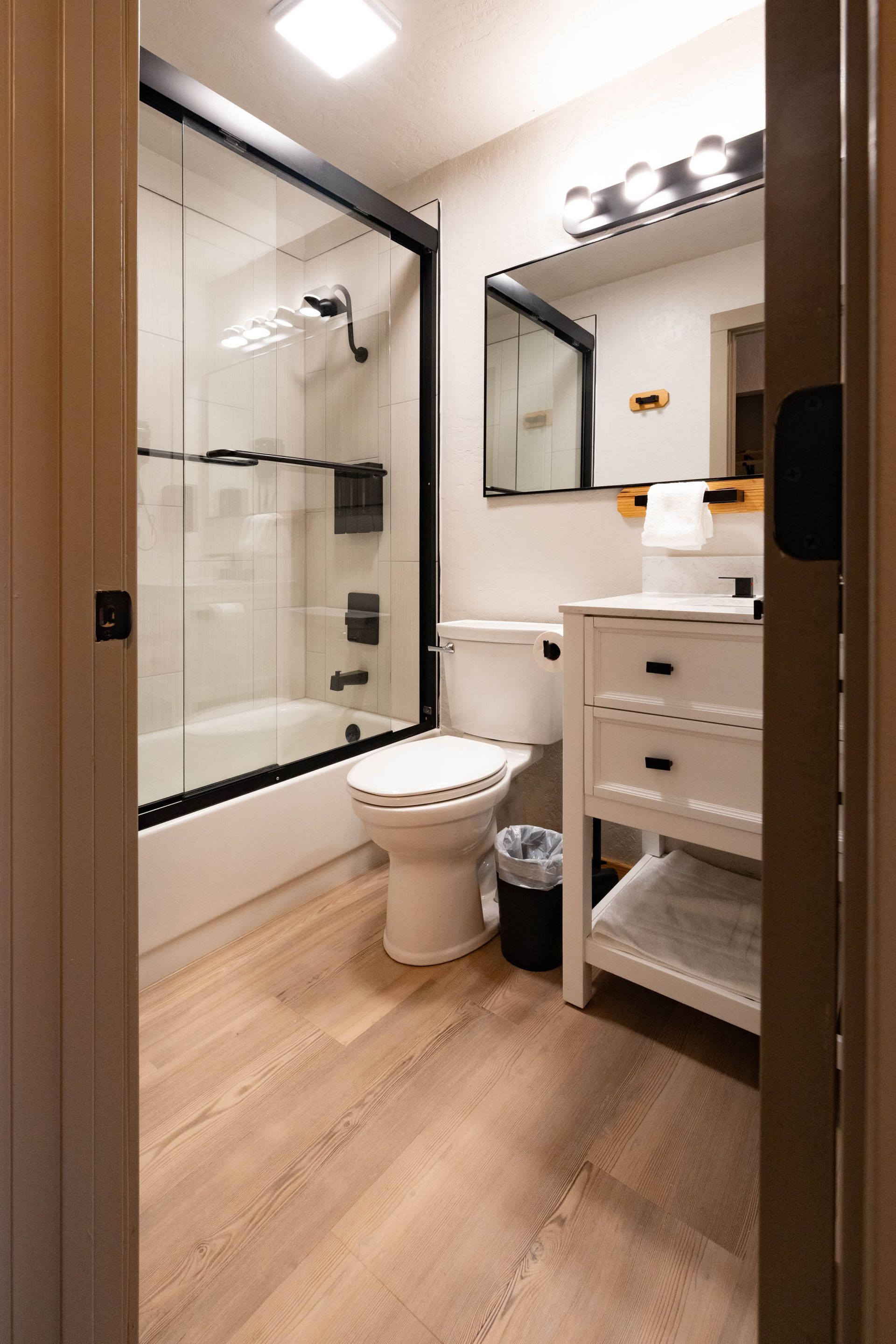 Bright modern bathroom with glass shower, toilet, vanity, and wood-look floor