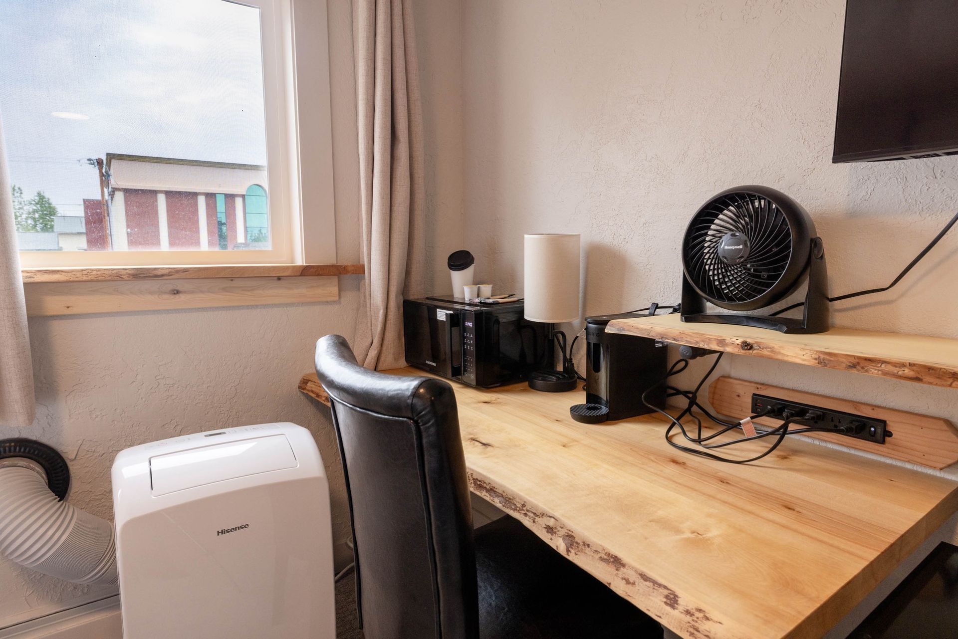 Home office desk by a window with a fan, monitors, and a portable air conditioner