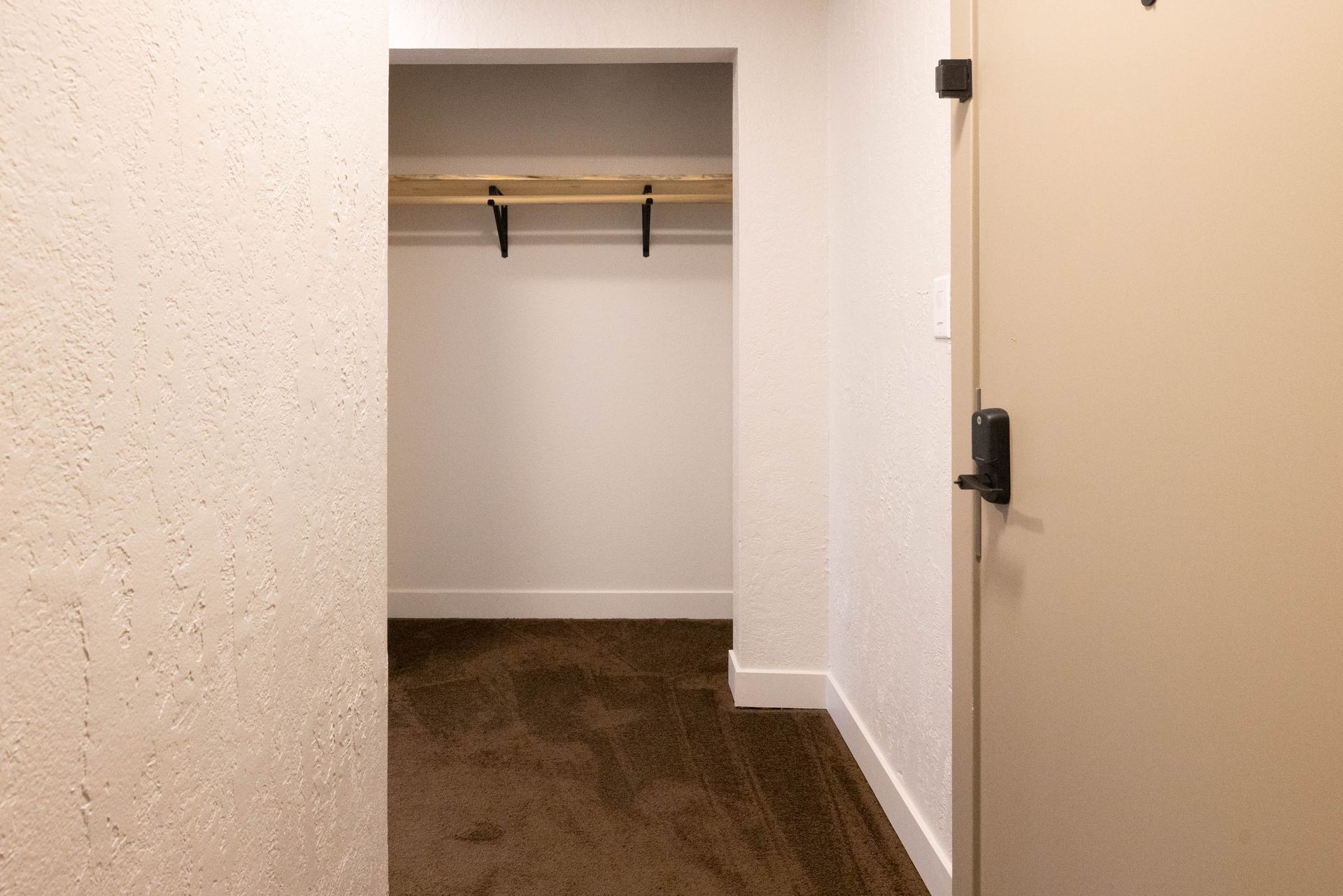 Empty closet with white walls, a wooden shelf, and dark flooring, viewed from a hallway