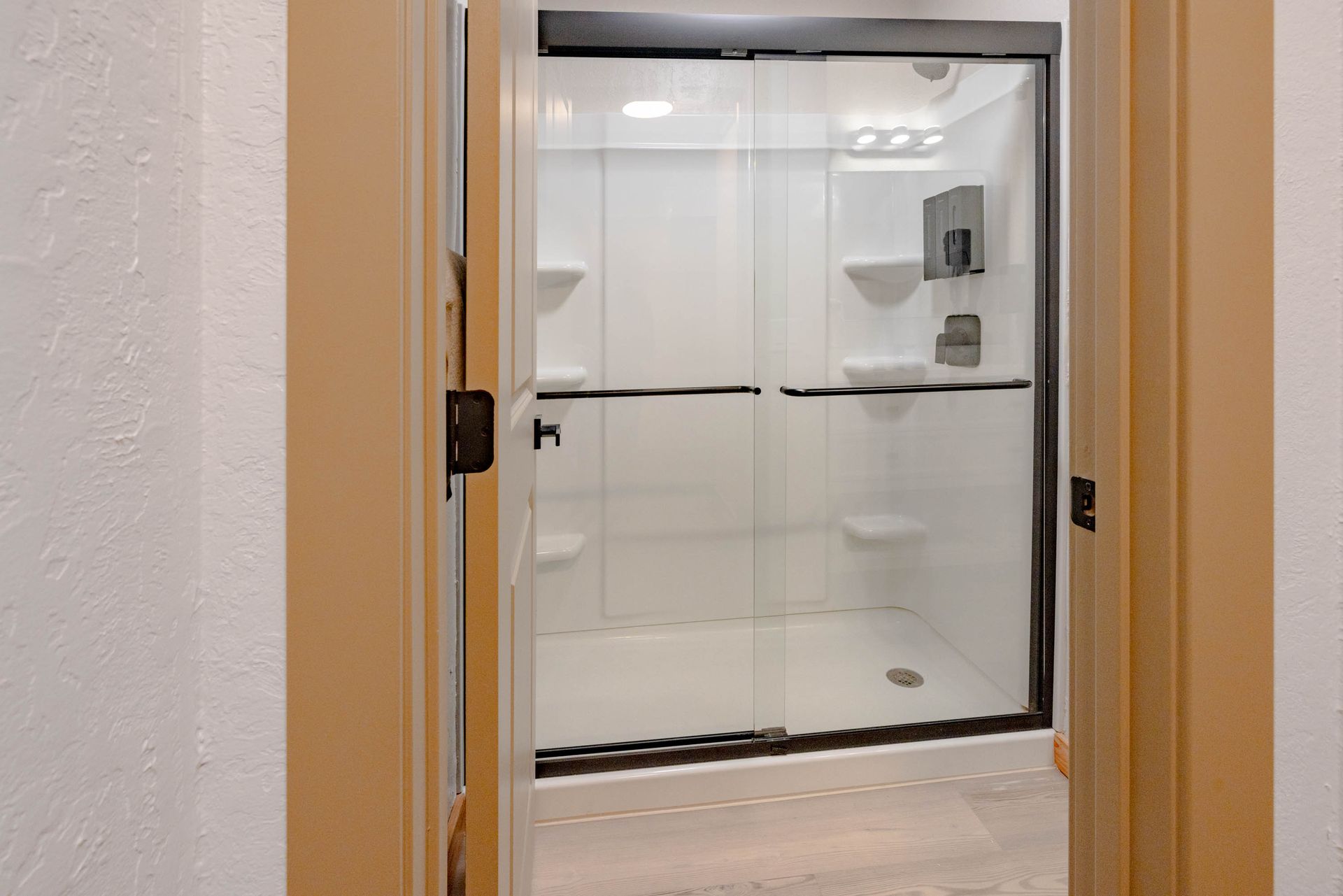Open doorway to a bright walk-in shower with white tile and black-framed glass door.