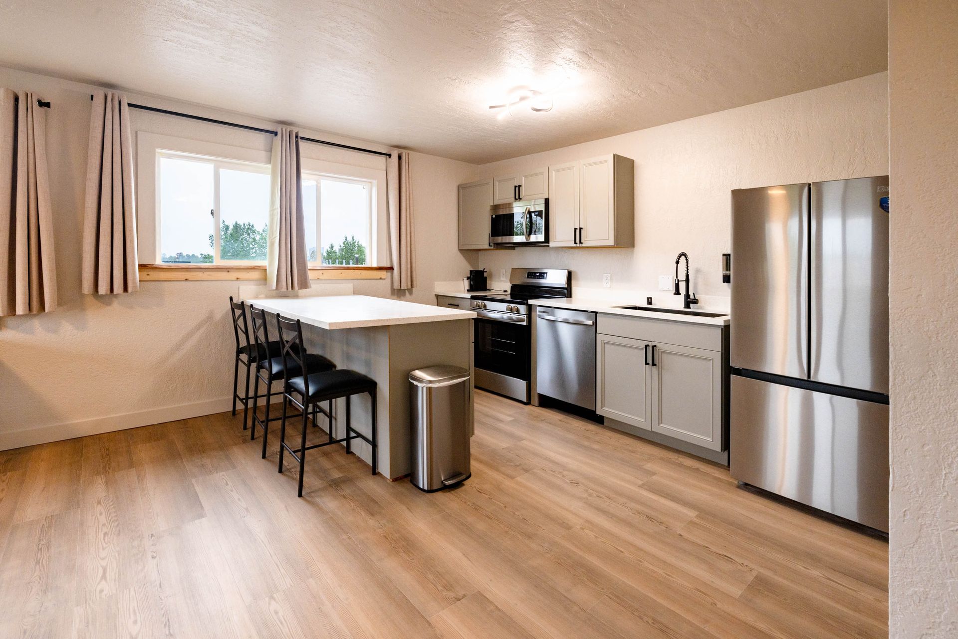 Modern kitchen and dining area with island, bar stools, stainless steel appliances, and wood flooring.