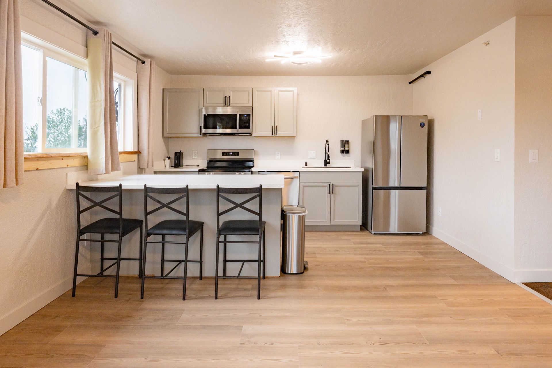 Bright modern kitchen with island, four black stools, white cabinets, and stainless steel refrigerator