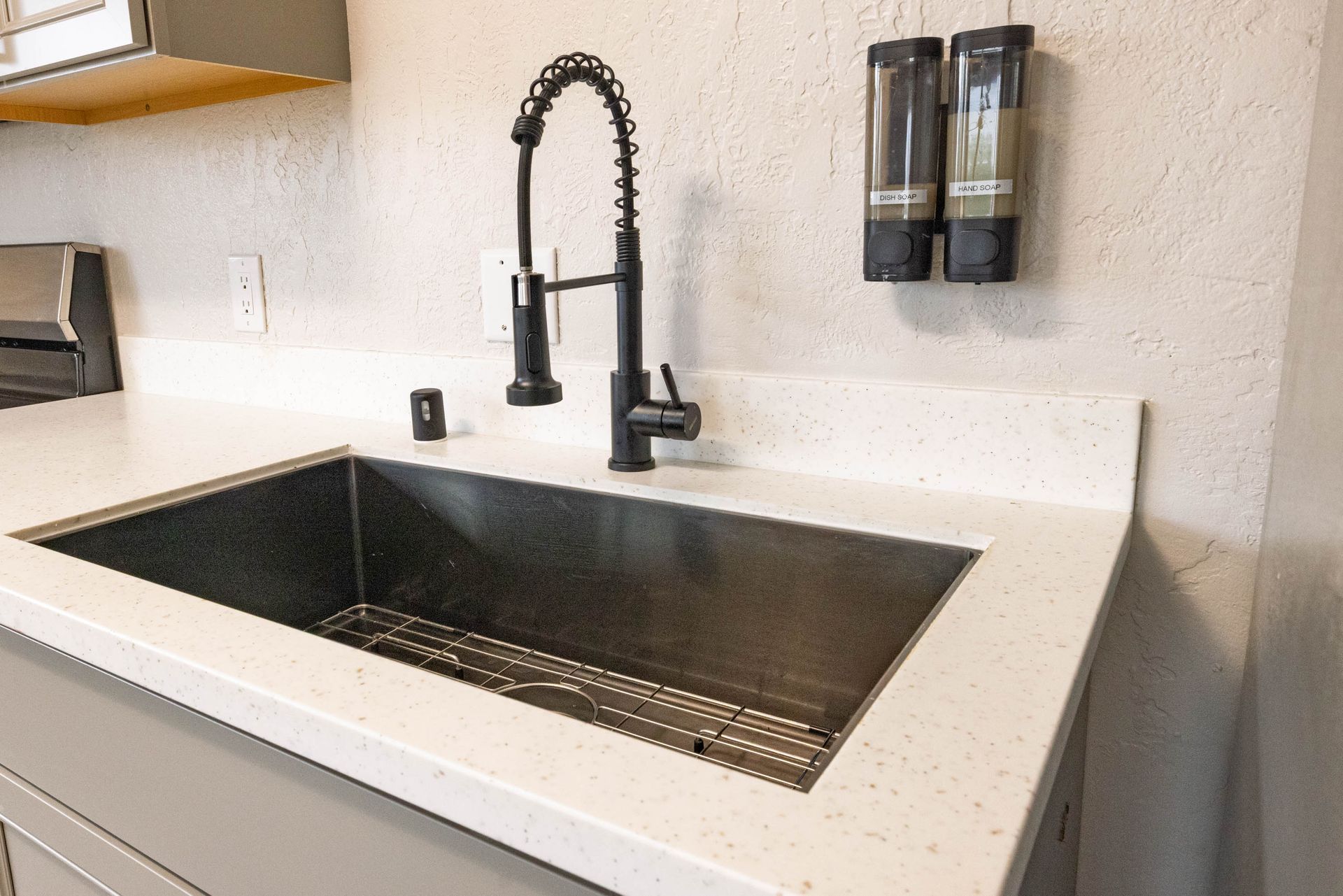 Modern kitchen sink with black faucet, dark basin, and white countertop against a light wall