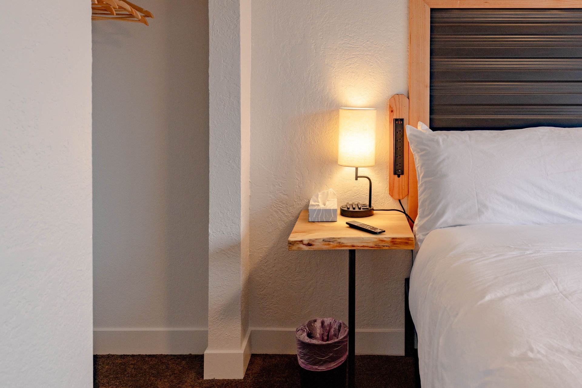 Cozy hotel room corner with bed, bedside table lamp, phone, and open closet