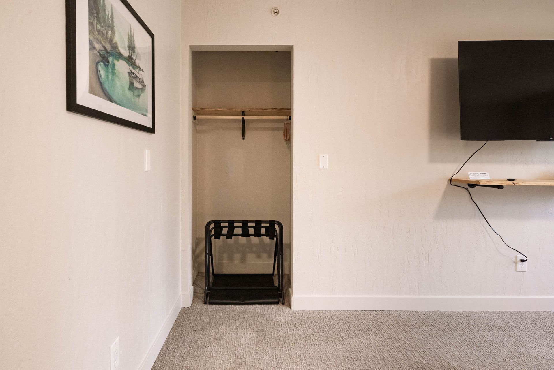 Empty bedroom with open closet, wall-mounted TV, and framed art on a light-colored wall.