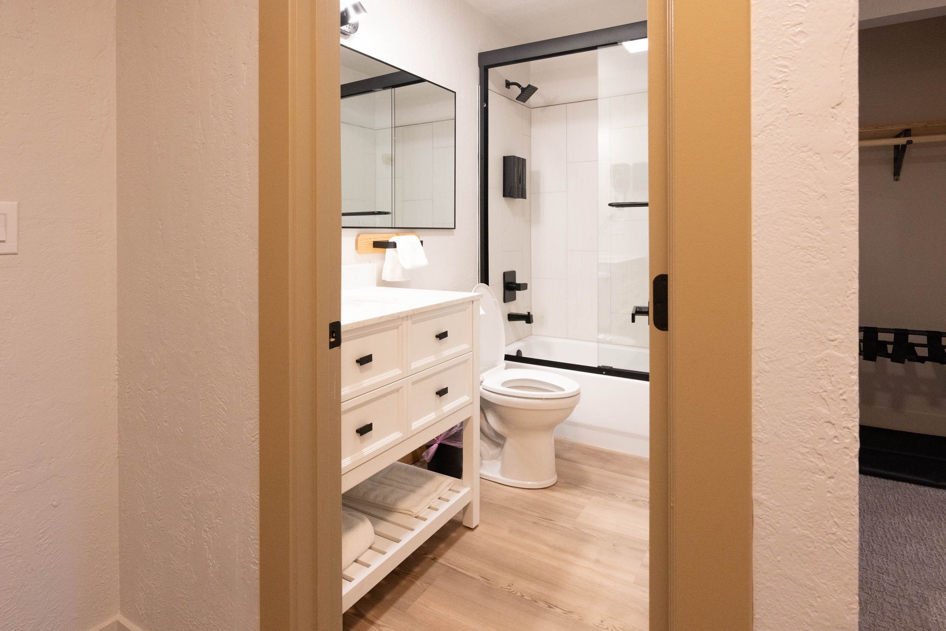 View through a doorway into a modern bathroom with white vanity, mirror, and toilet.