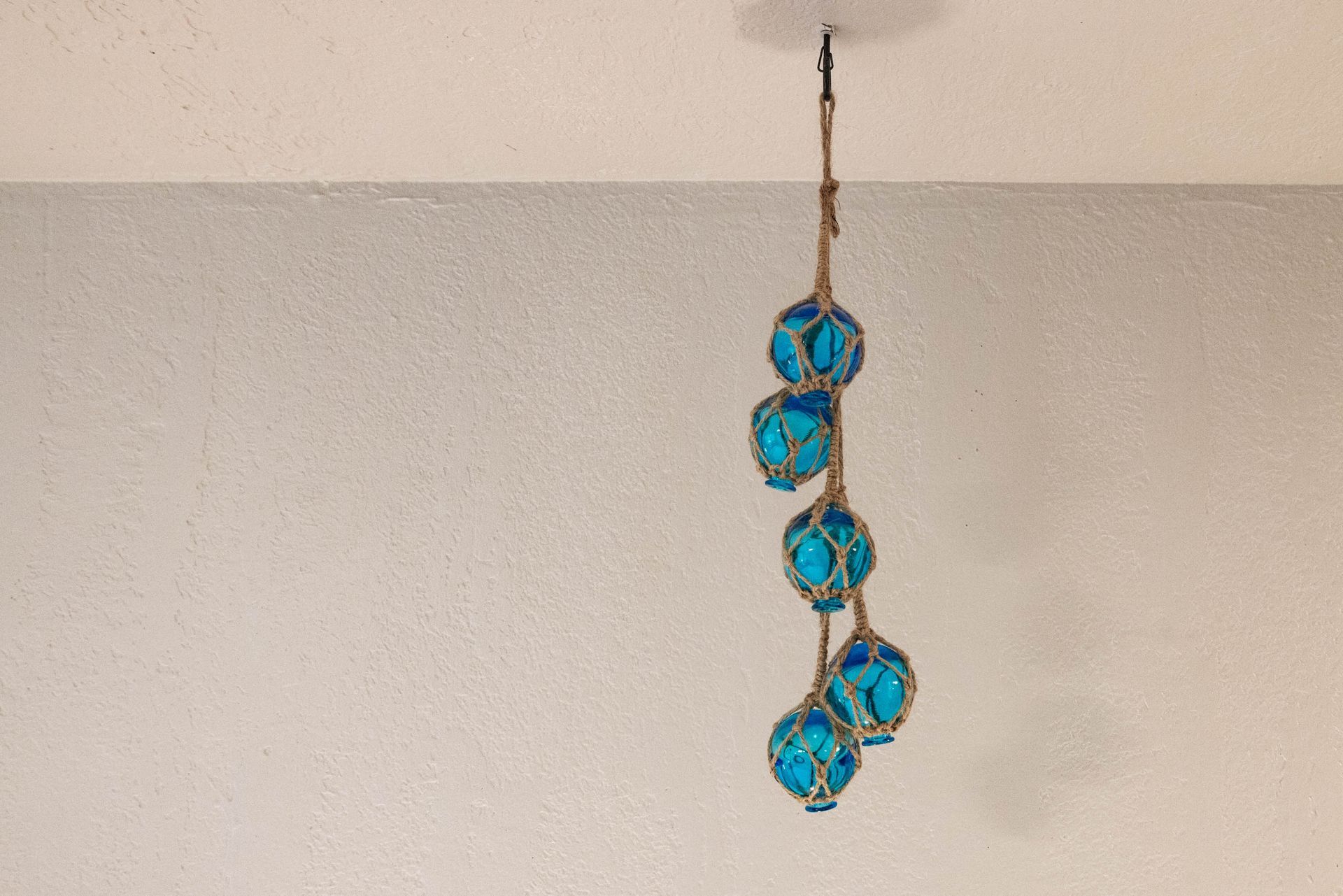 Blue and turquoise hanging decorative ornament on a beige wall near the ceiling