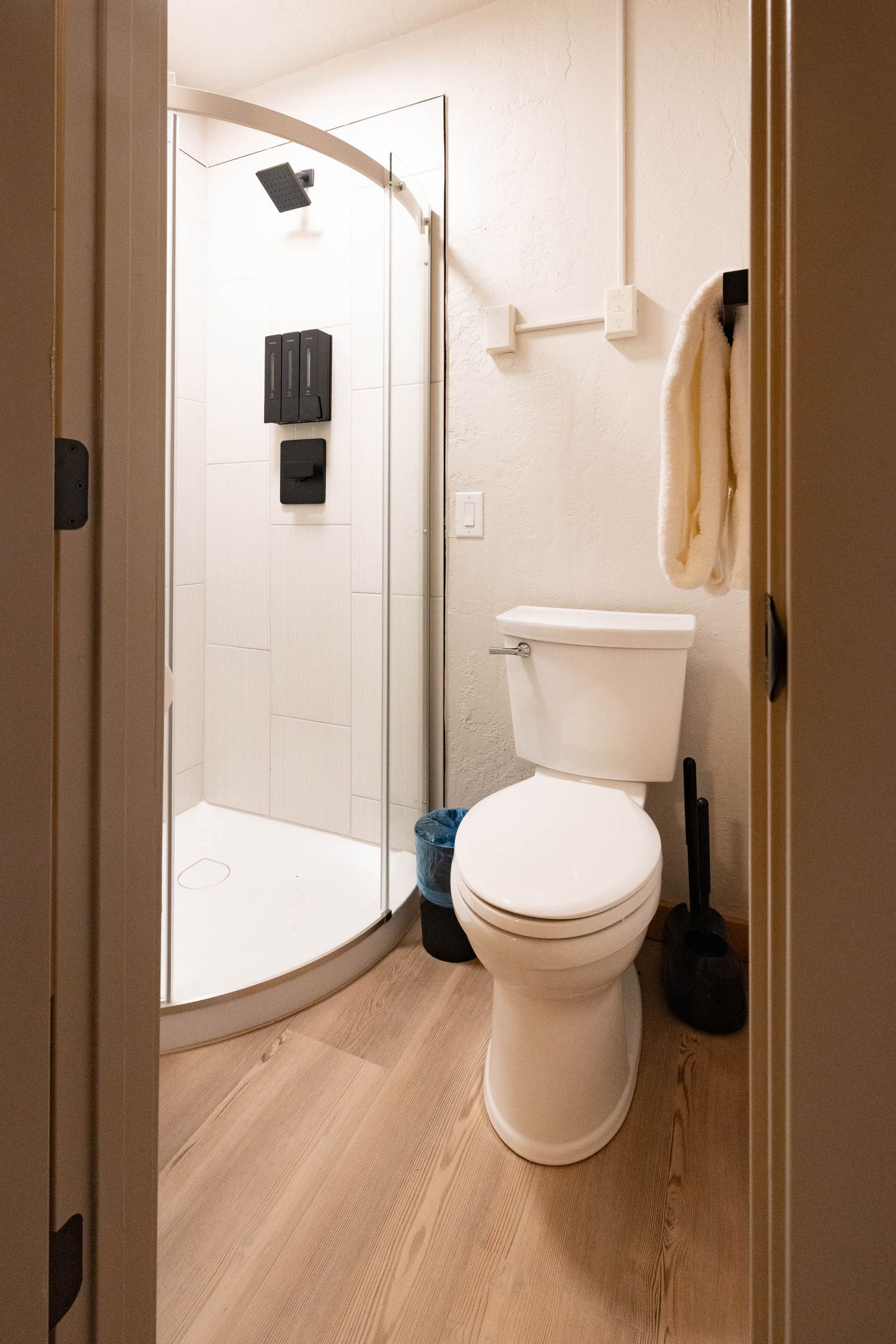 Small bathroom with a white toilet, curved shower door, and beige walls and floor.