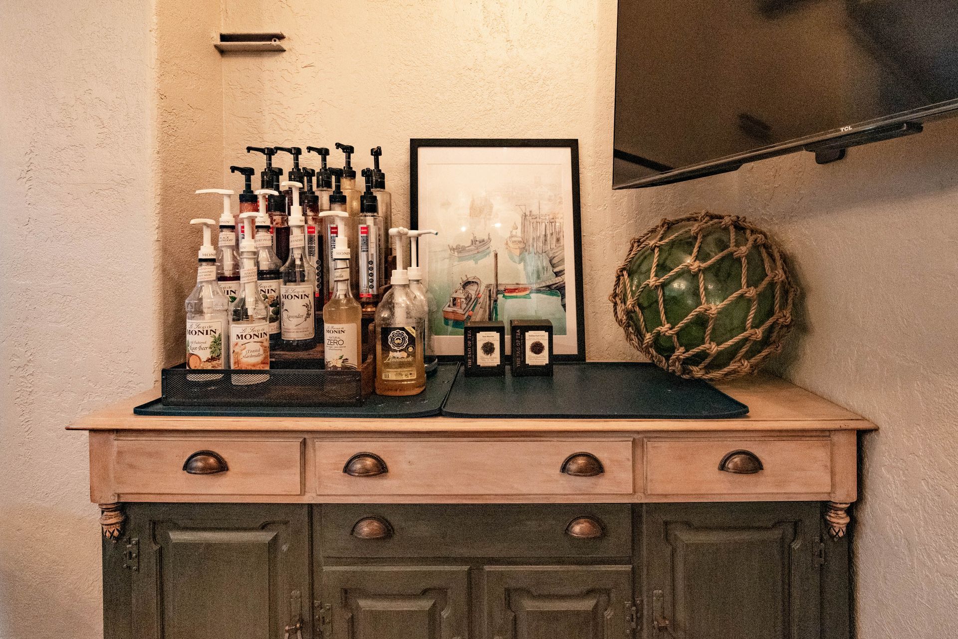Decorative bar cabinet with bottles, framed art, and a green woven orb on a tabletop