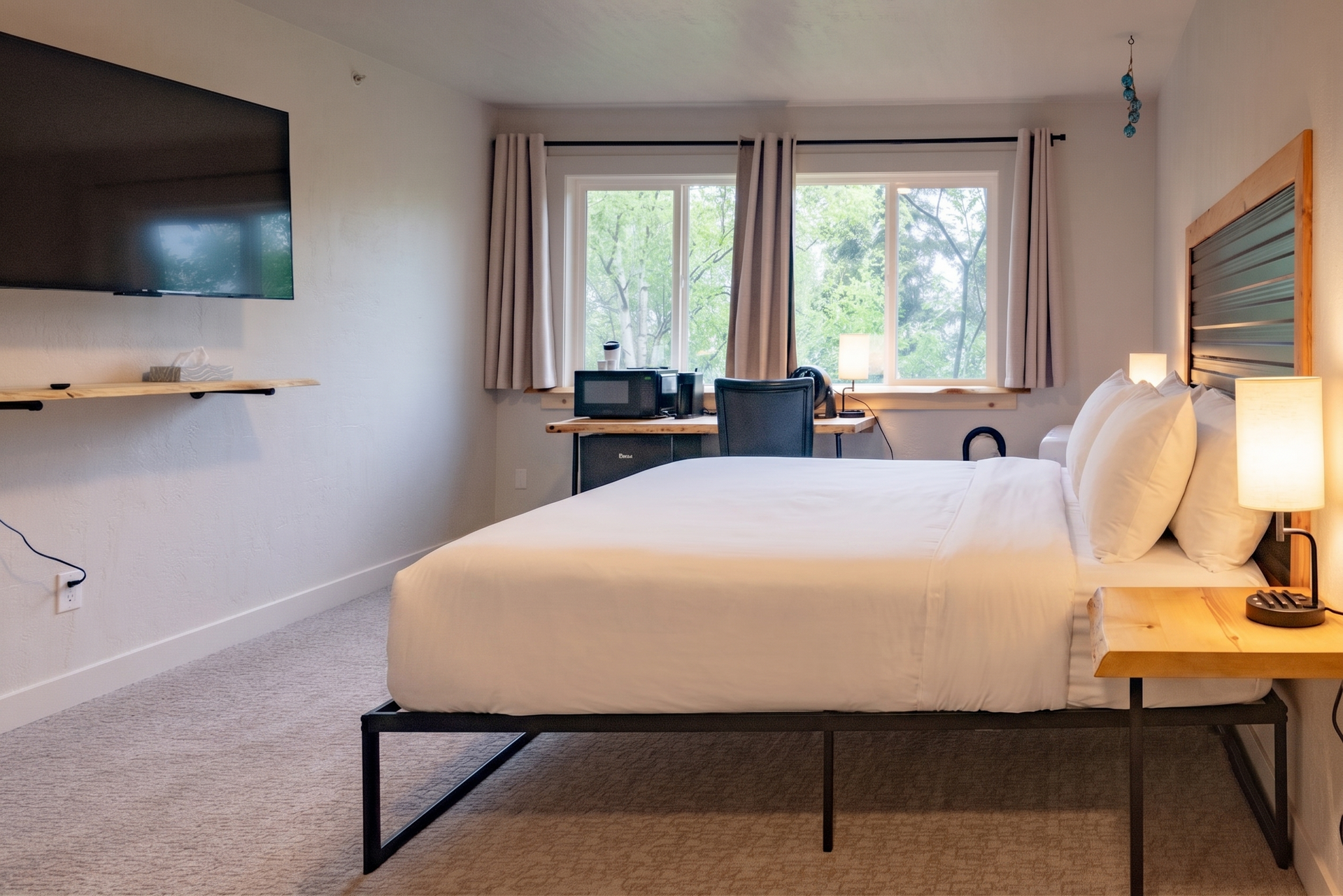 Modern bedroom with a bed, wall-mounted TV, desk, and large window with curtains.