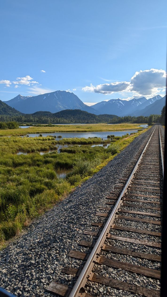 Railroad tracks beside a marshy valley with mountains and blue sky in the distance
