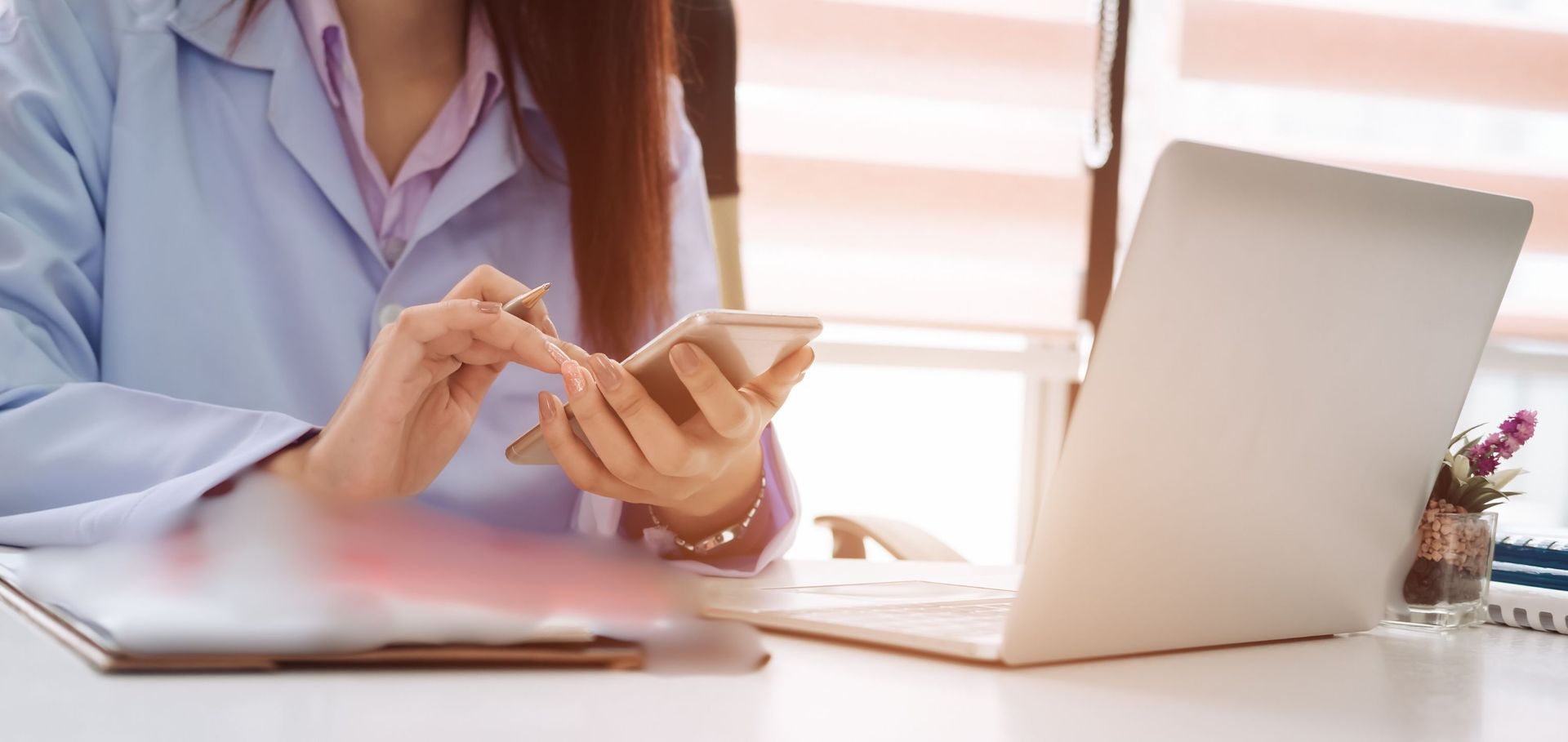 a woman is sitting at a desk using a laptop and a cell phone .