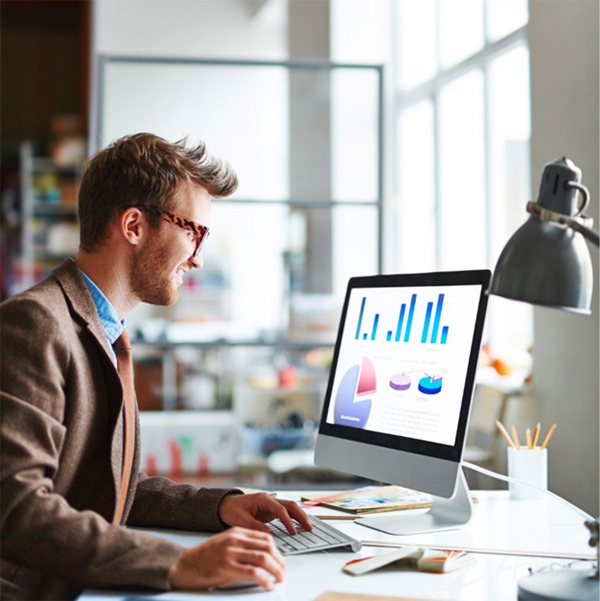 A man is sitting at a desk using a computer with a graph on the screen.