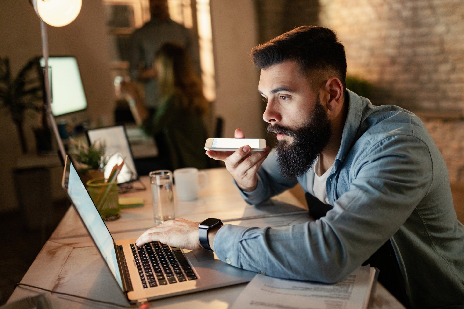 A man holding a phone and looking at a laptop