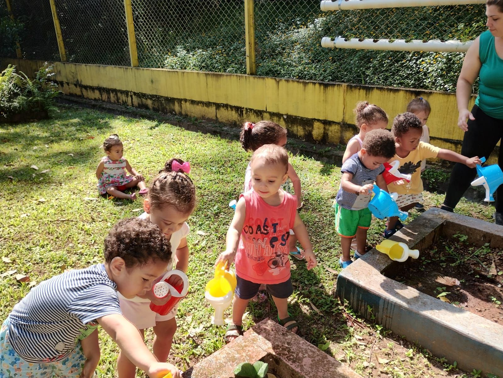 Um grupo de crianças está brincando em uma caixa de areia com regadores.