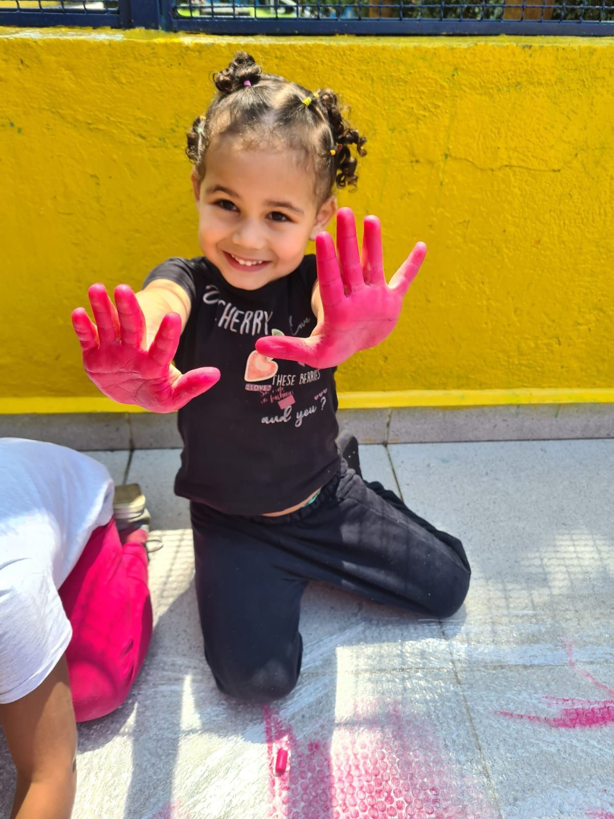 Uma menina está ajoelhada com as mãos pintadas de rosa