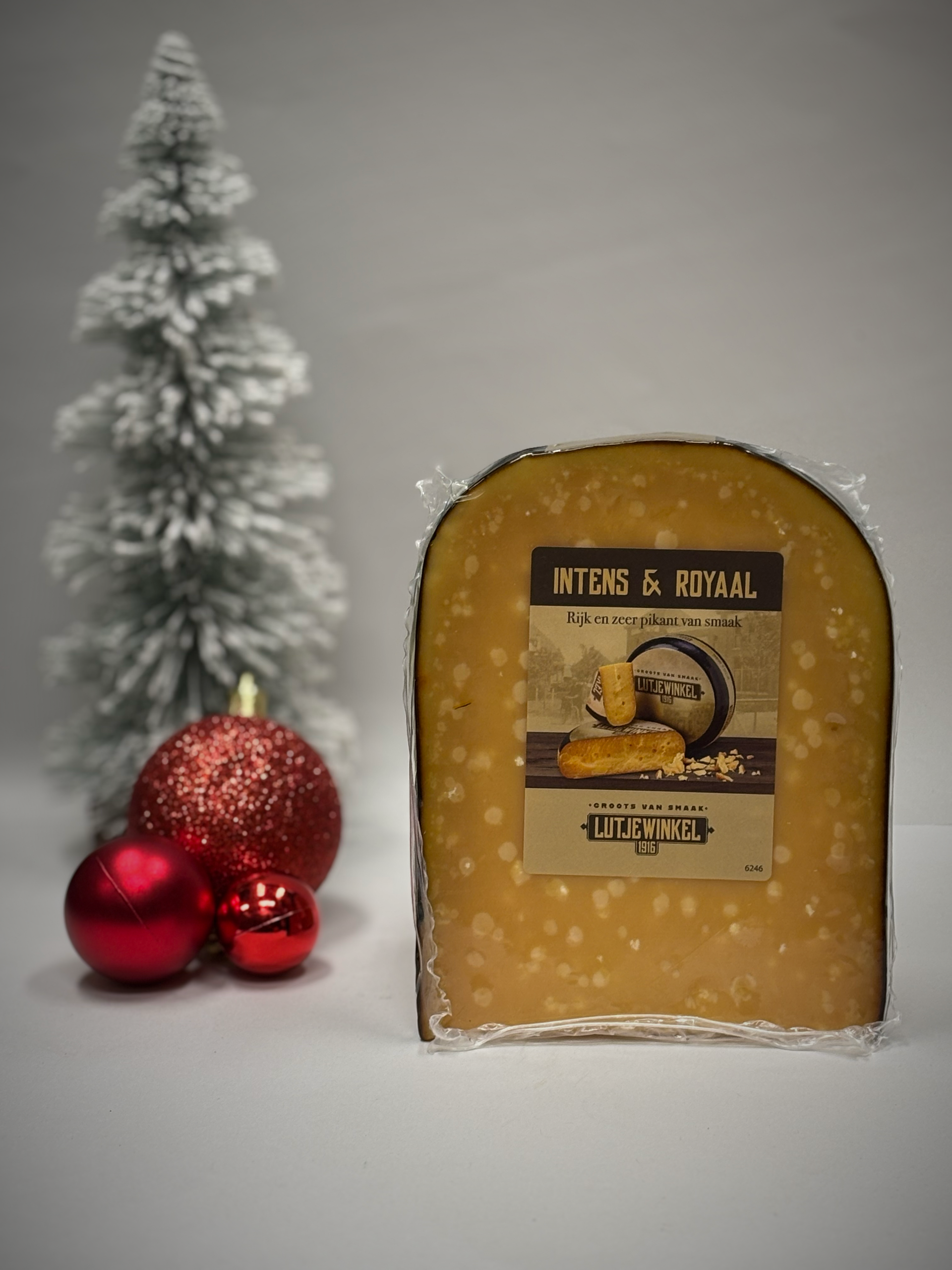 Een punt kaas met een etiket, naast een kleine kerstboom en ornamenten.