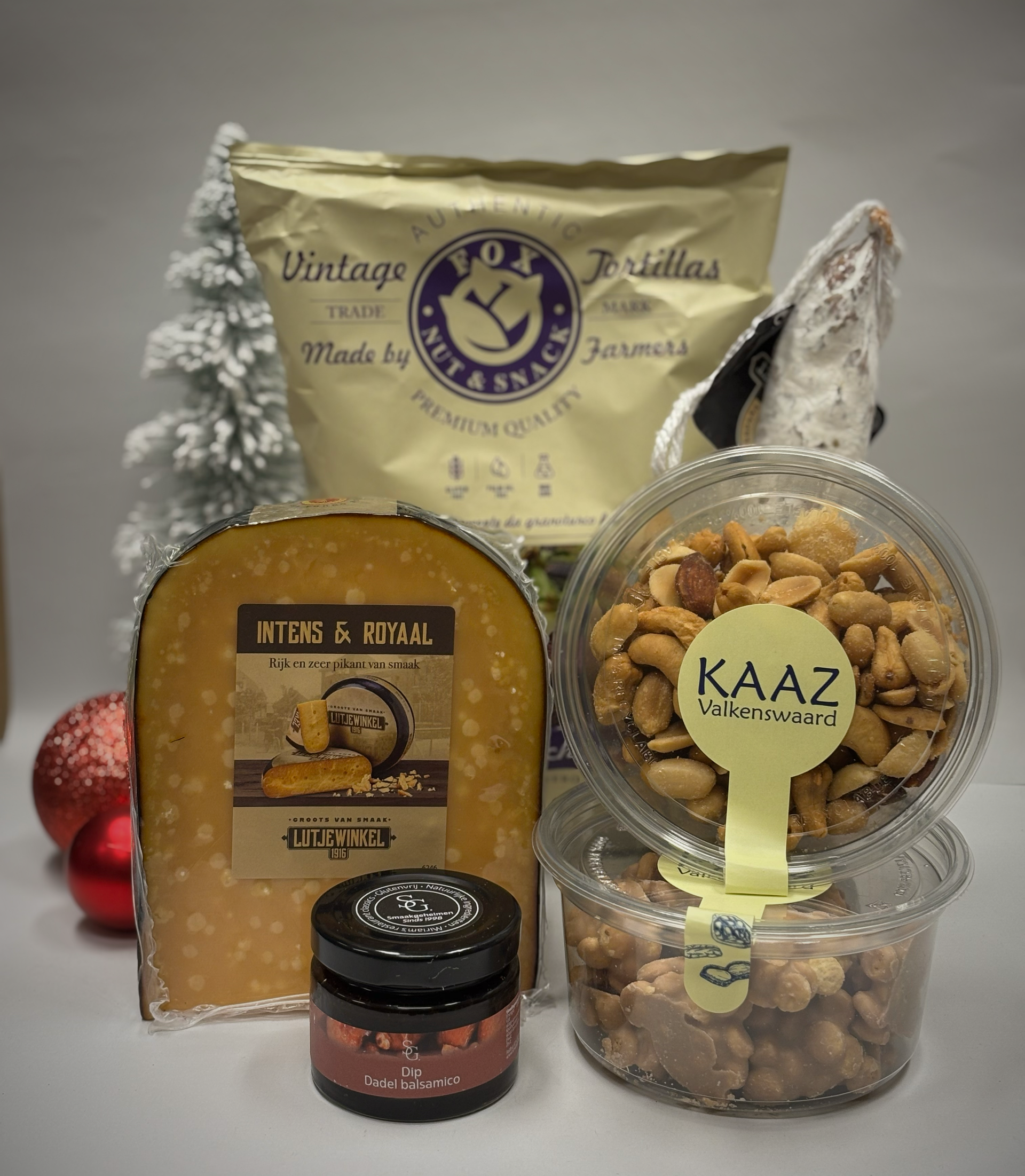 Heerlijke geschenkmand met kaas, noten, crackers en jam. Kerstboom en ornamenten op de achtergrond.
