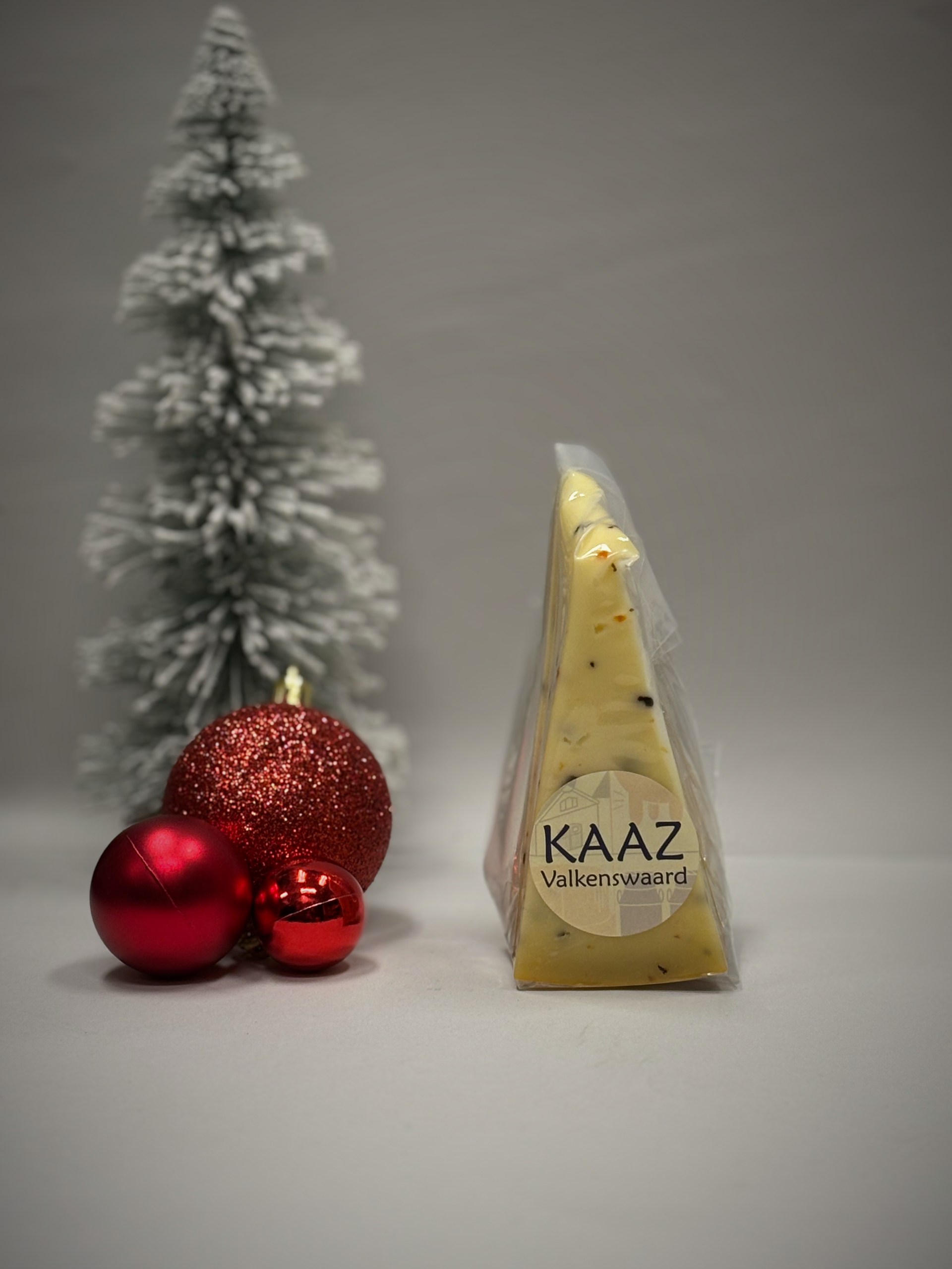Kaaspuntje in verpakking met rode kerstversiering en een klein versierd boompje.